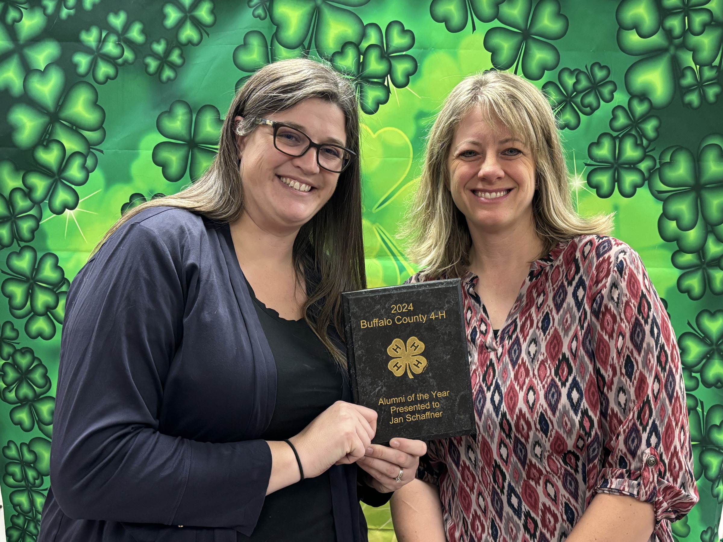 Picture of Annie and Jan with an award in front of a green clover background.