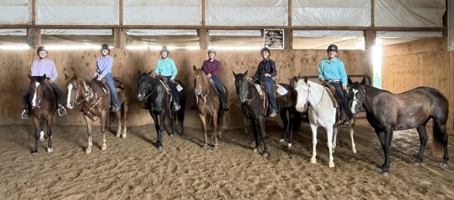 Six youth exhibitors posing on horses in horse arena.